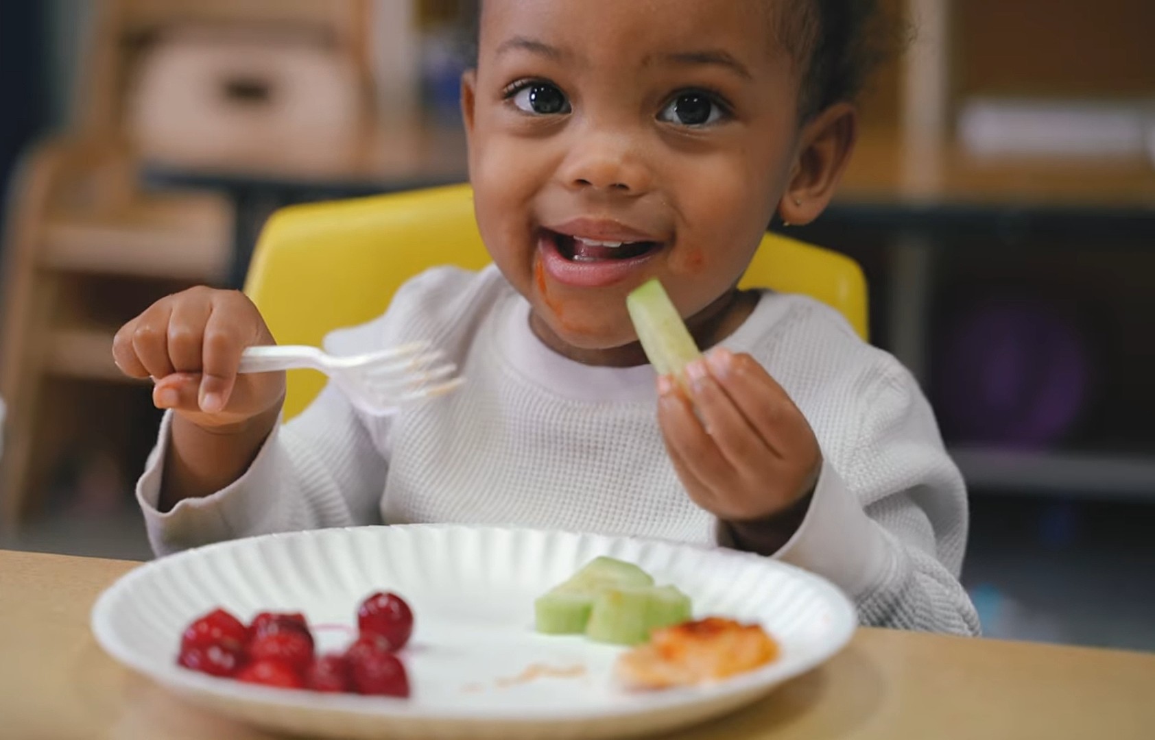 Smiling toddler enjoying fresh fruit and vegetables at lunch
