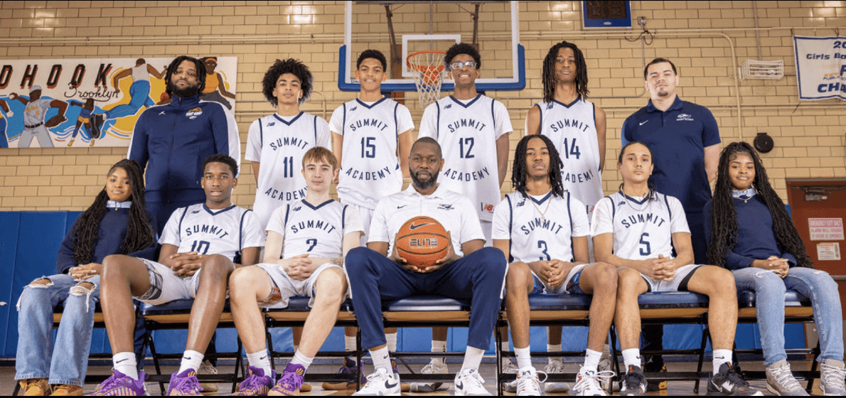 A basketball team posing in a gym with their coach holding a basketball.