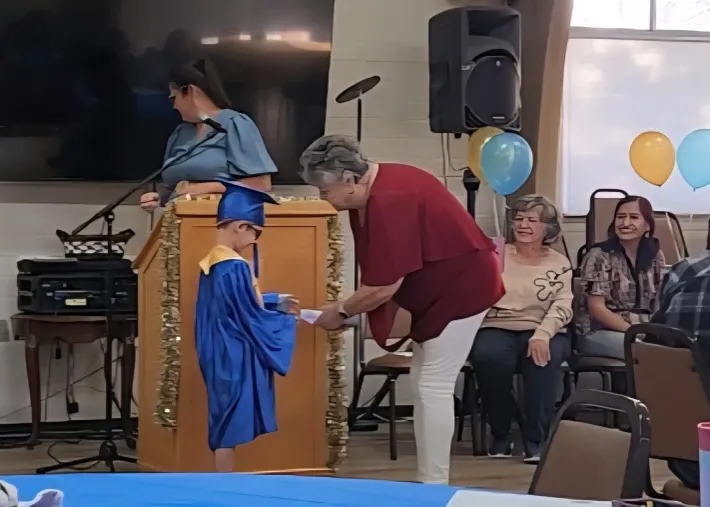 A child in cap and gown receiving a certificate at the graduation ceremony